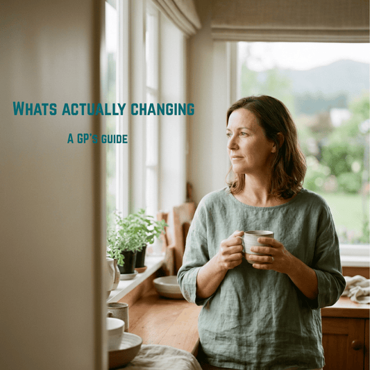 New Zealand woman in her late 40s holding a mug of tea by a kitchen window, looking calmly out — perimenopause in your 40s