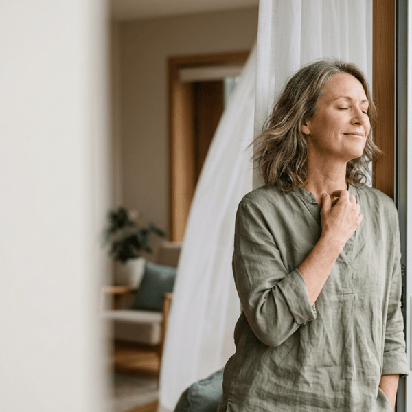 Woman around 50 cooling by an open window, looking relieved — hot flushes natural support